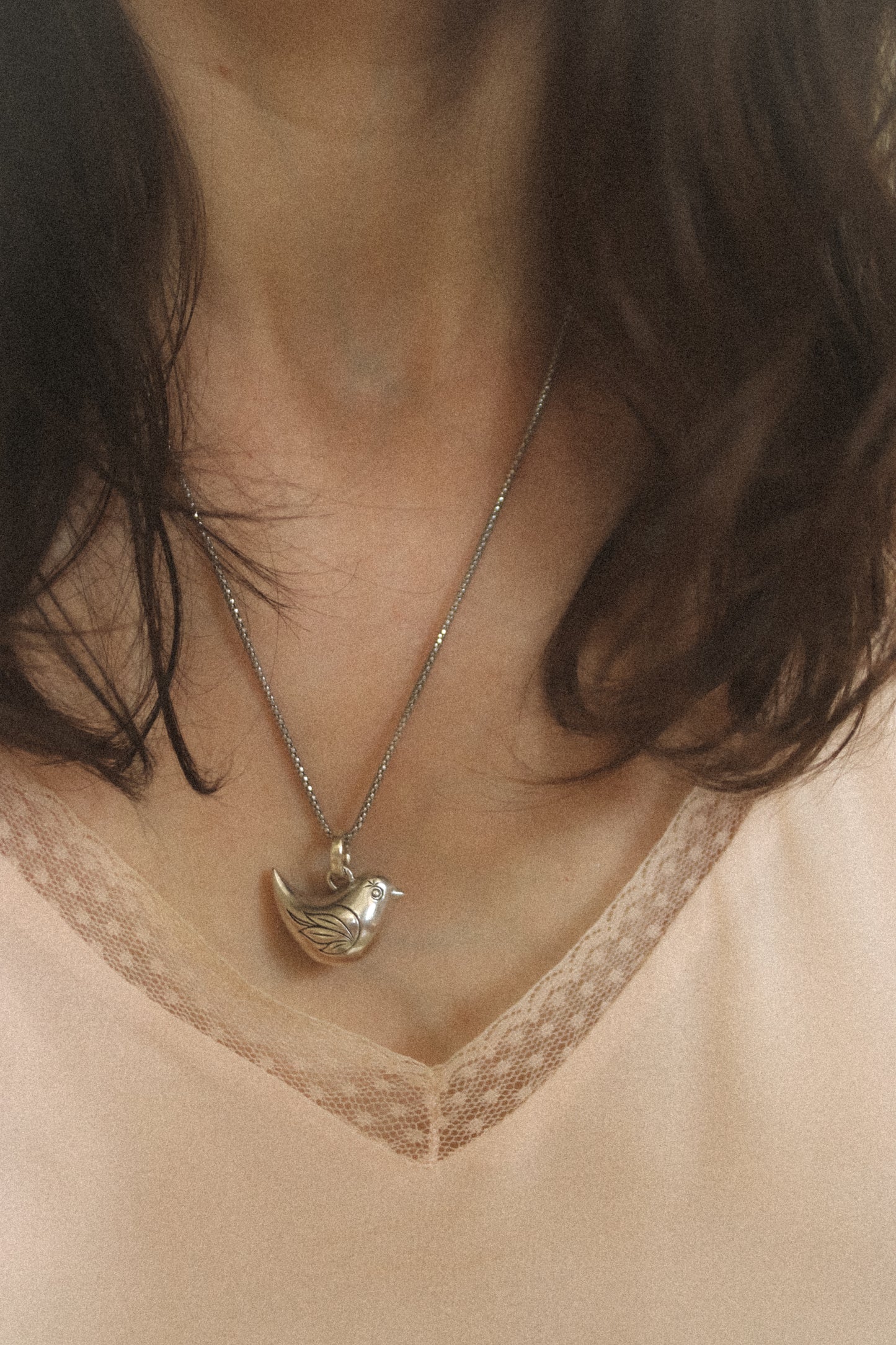 Close-up of a necklace with a pendant worn by a person with dark hair and a light-colored top.