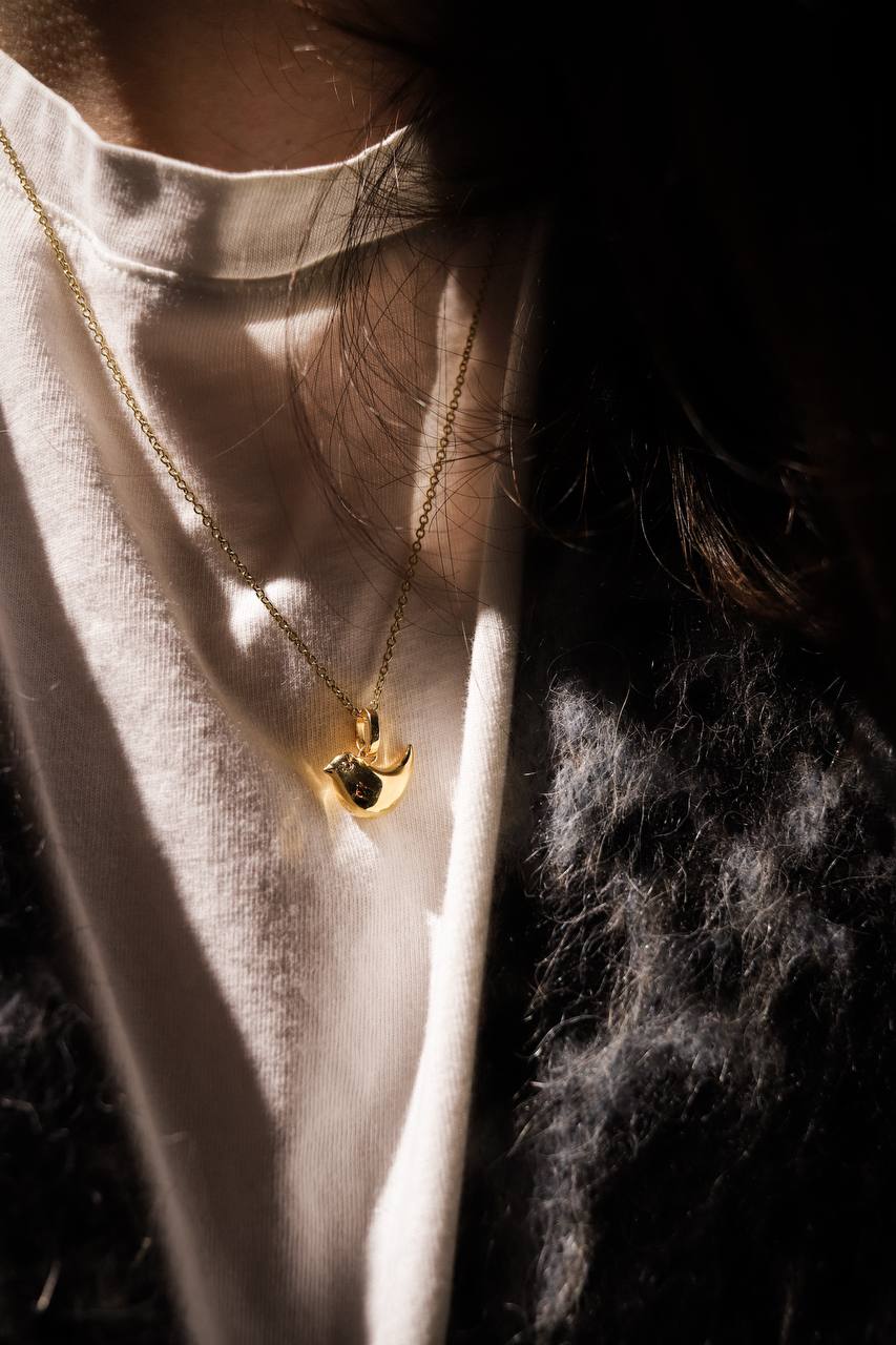 Close-up of a gold necklace with a pendant on a white shirt.