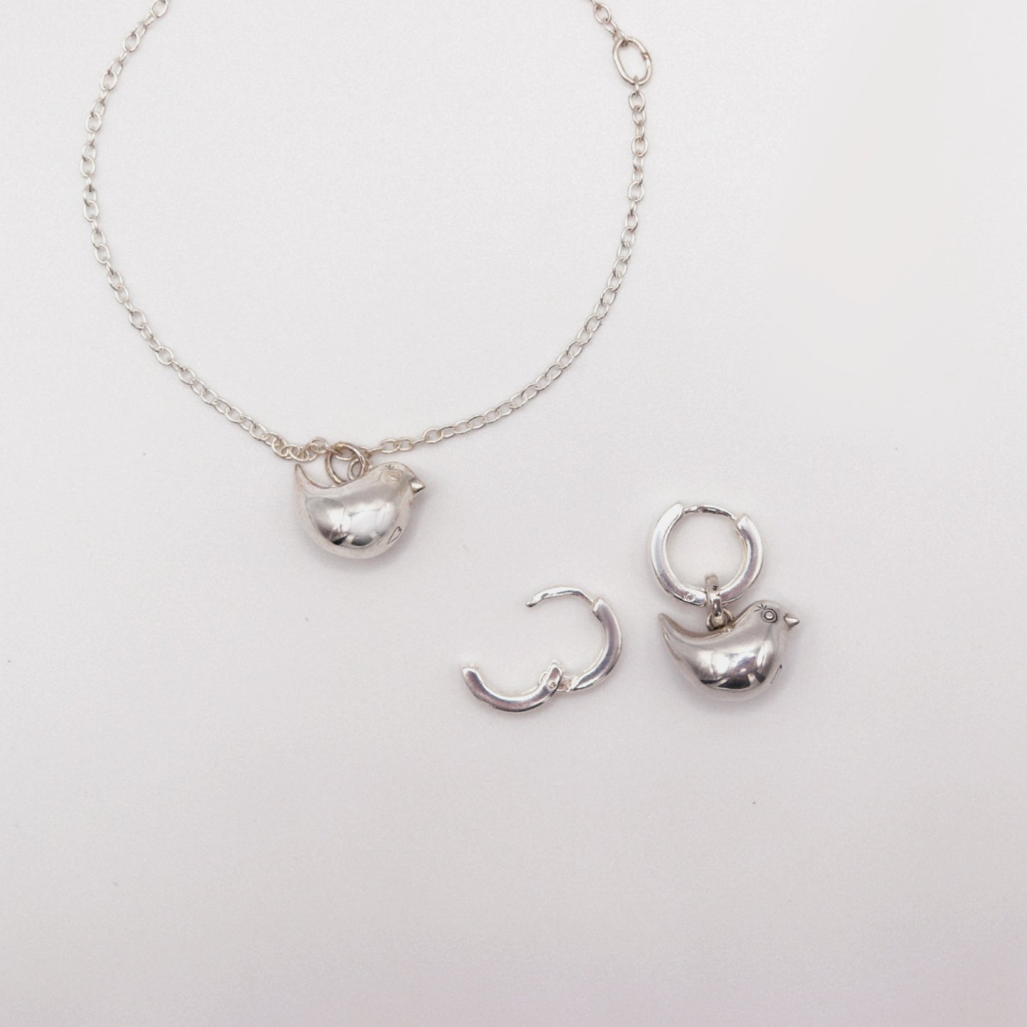 Silver necklace with pendant and hoop earrings on a light gray background