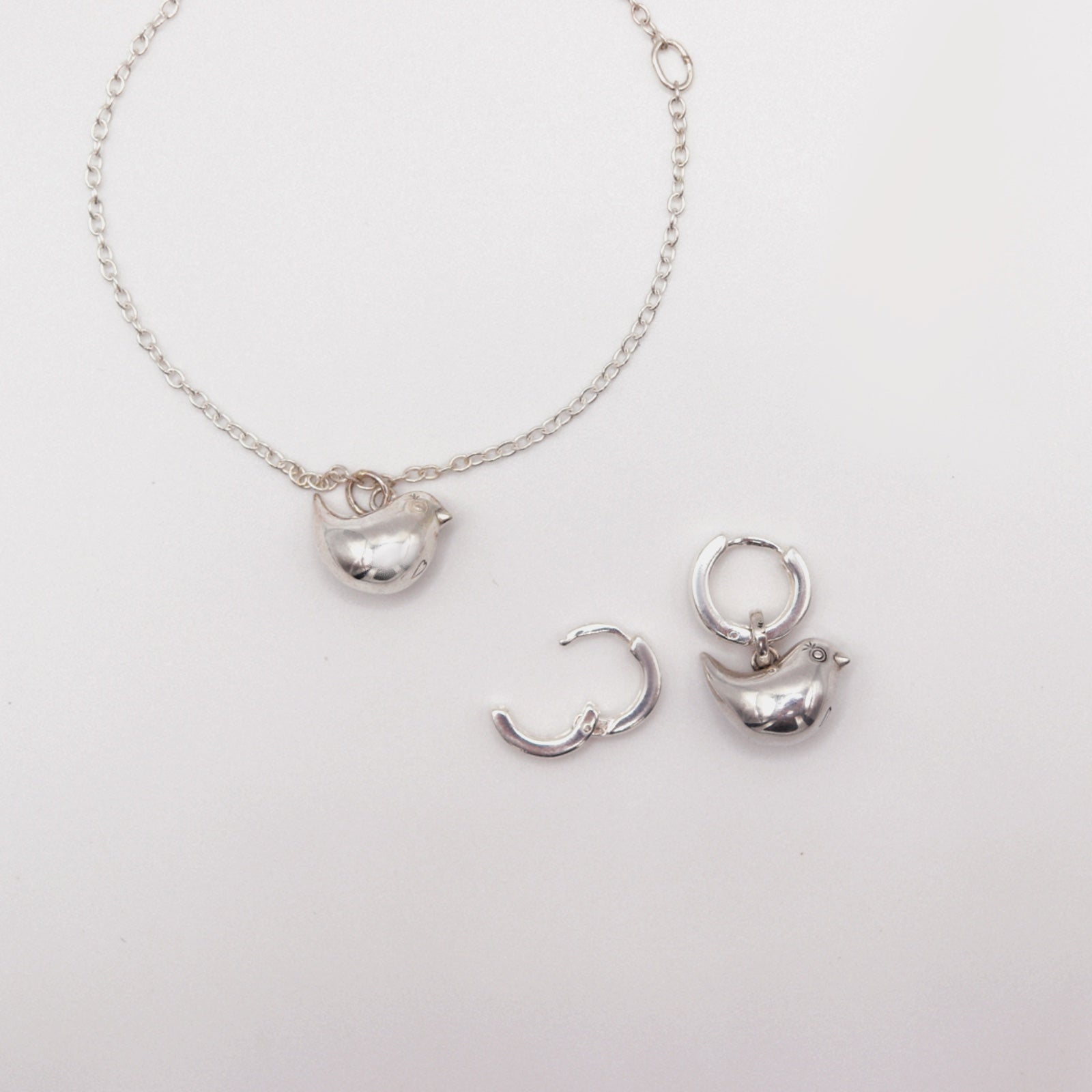 Silver necklace with pendant and hoop earrings on a light gray background
