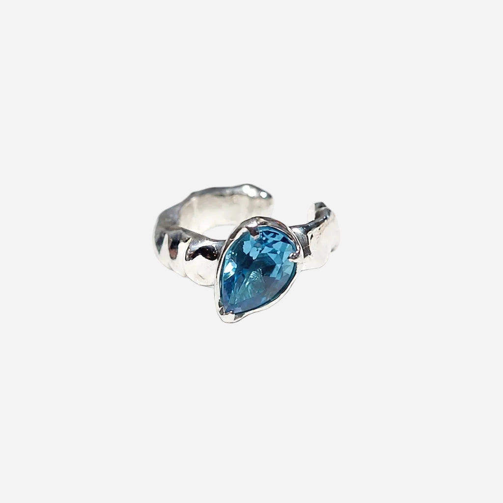 A silver-toned ring featuring a teardrop-shaped blue gemstone, photographed on a seamless white background.