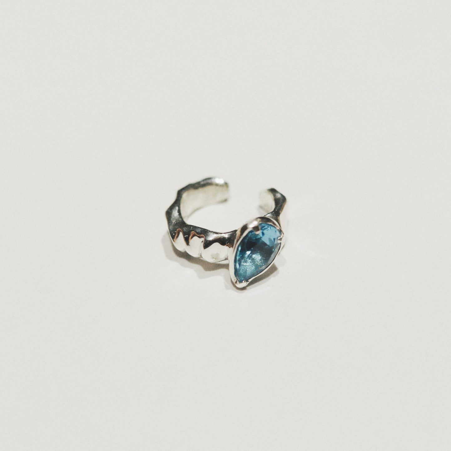 A small silver-toned ring with a textured, organic shape and a marquise-cut light blue gemstone, shown on a plain off-white background.