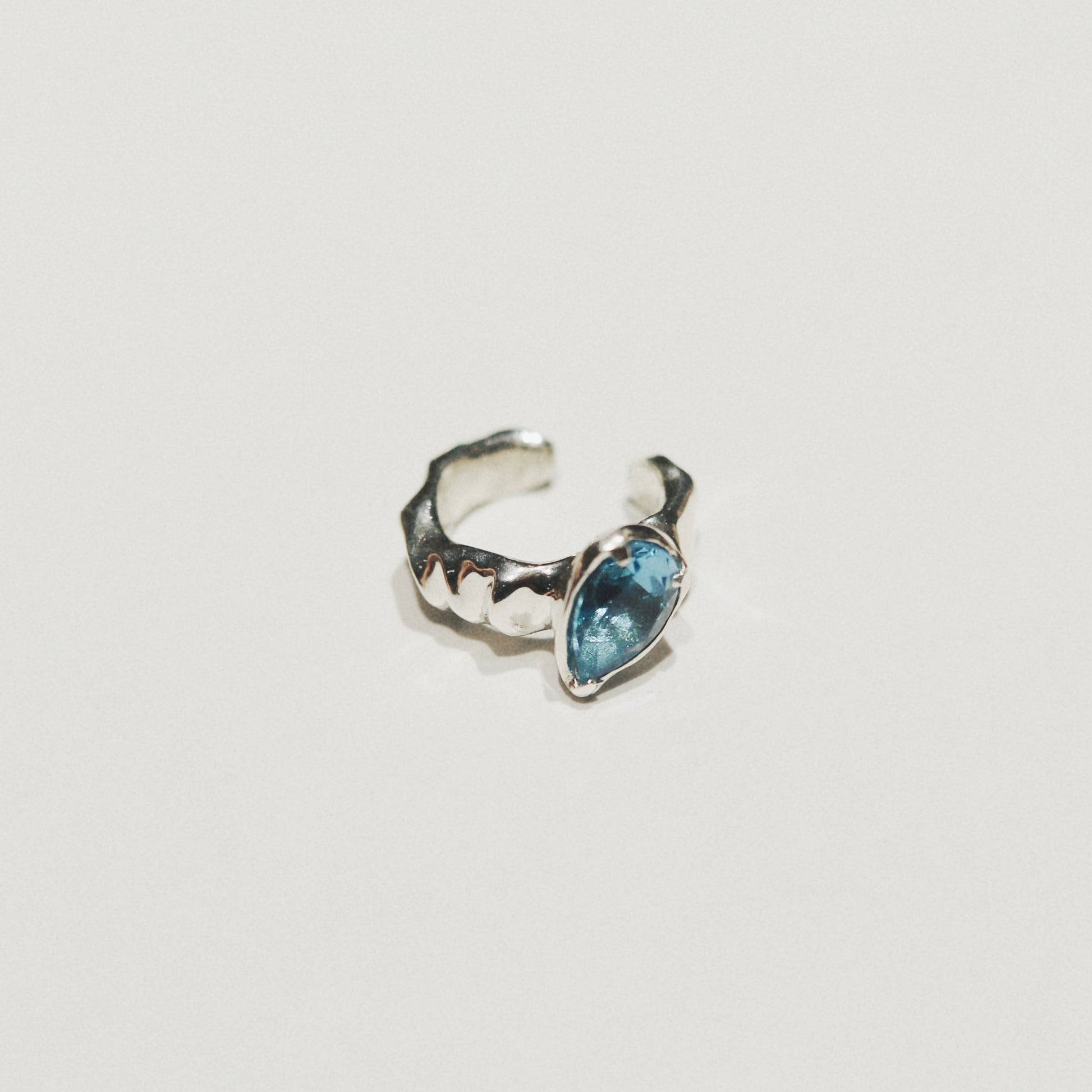 A small silver-toned ring with a textured, organic shape and a marquise-cut light blue gemstone, shown on a plain off-white background.