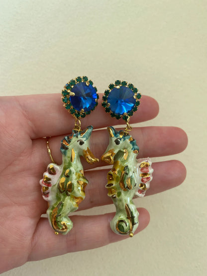 Seahorse earrings with blue gemstones held in a hand against a beige background