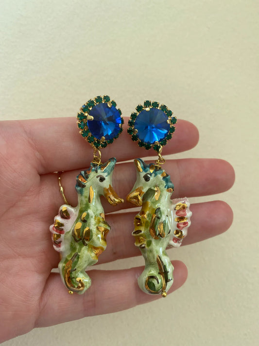 Seahorse earrings with blue gemstones held in a hand against a beige background