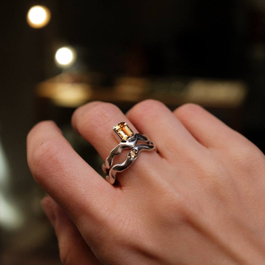 Hand wearing a silver ring with a yellow gemstone against a blurred background