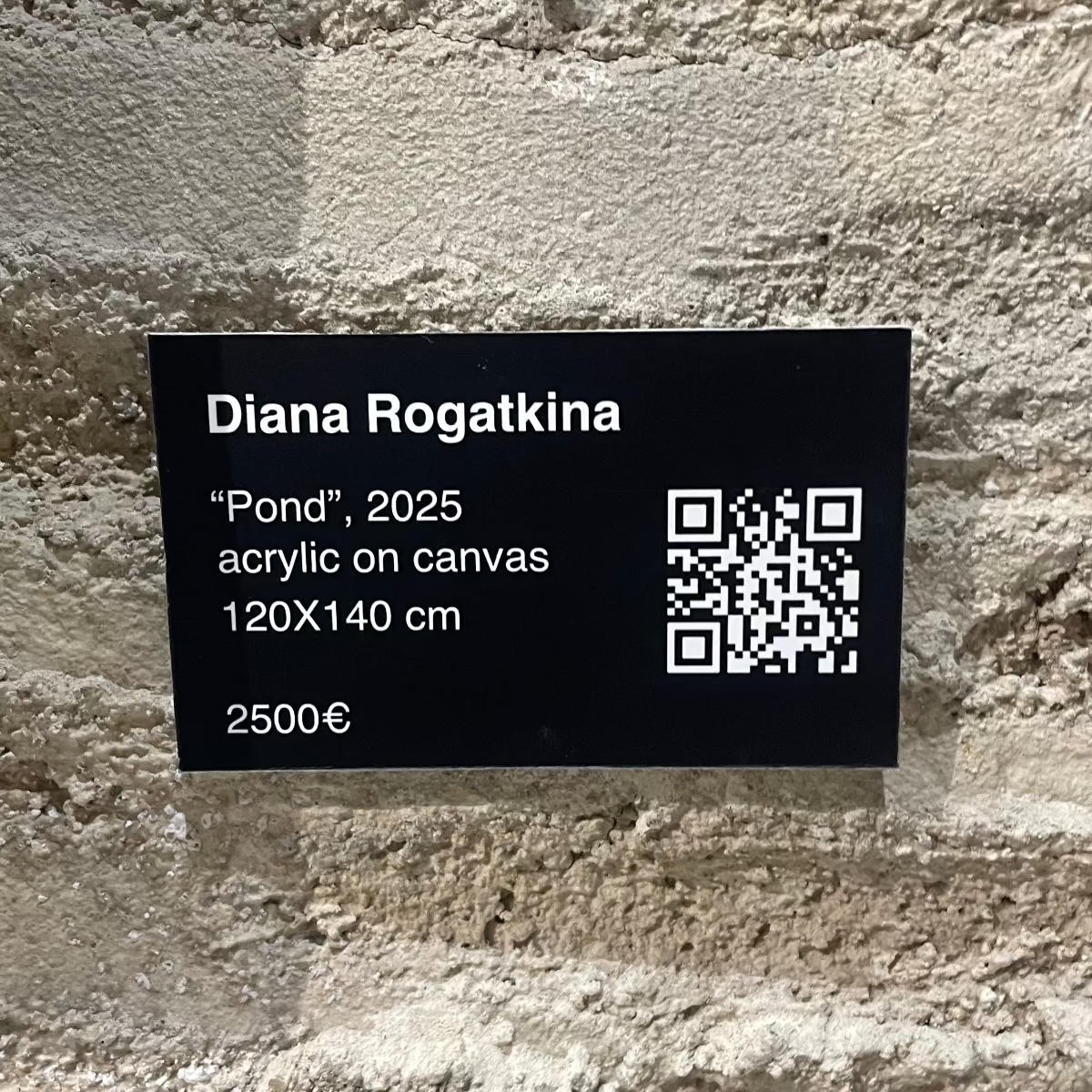 A black informational plaque mounted on a textured stone wall, displaying details for Diana Rogatkina's 'Pond', 2025 acrylic on canvas print, 120x140 cm, priced at 2500€. The plaque includes a QR code.