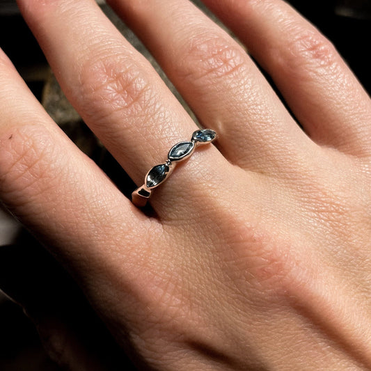 Close-up of a hand wearing a ring with blue gemstones on a blurred background