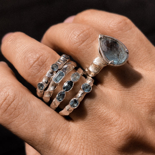 Close-up of a hand wearing multiple silver rings with gemstones on a dark background