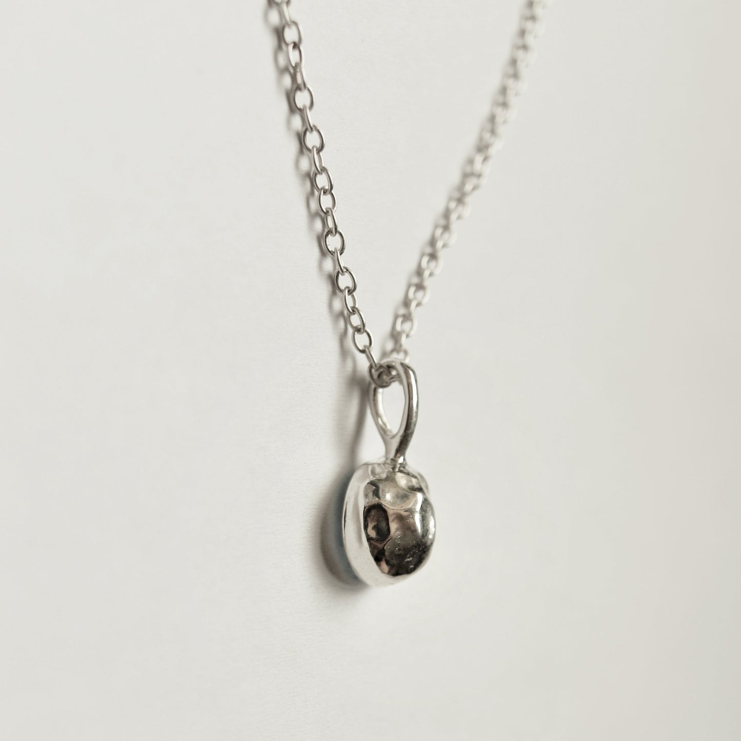 A silver chain necklace with a small, polished silver pendant, photographed against a clean, off-white background.