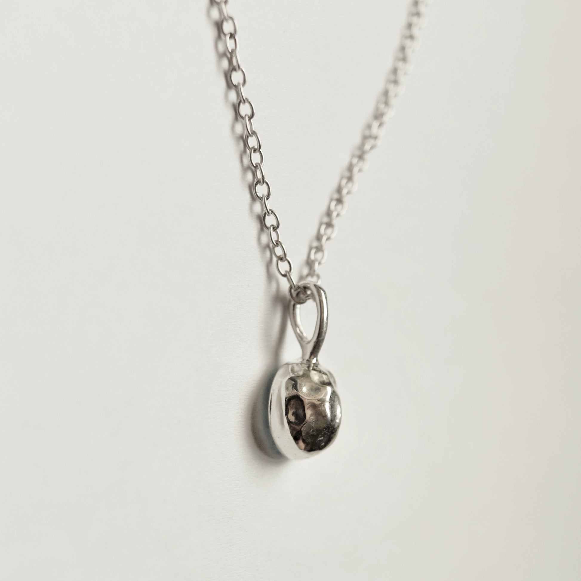 A silver chain necklace with a small, polished silver pendant, photographed against a clean, off-white background.