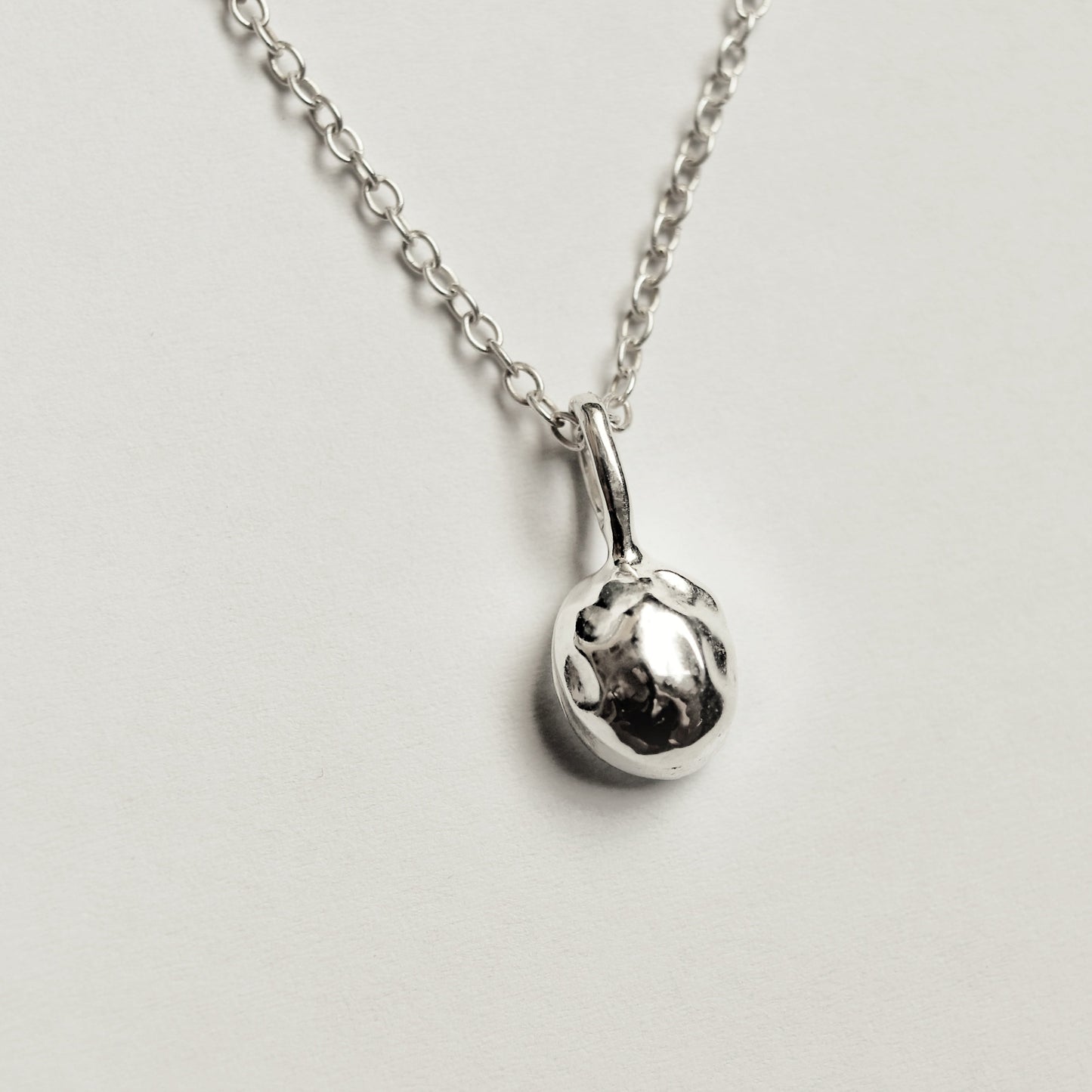 A silver chain necklace with a small, polished spherical pendant, photographed against a plain light gray background.