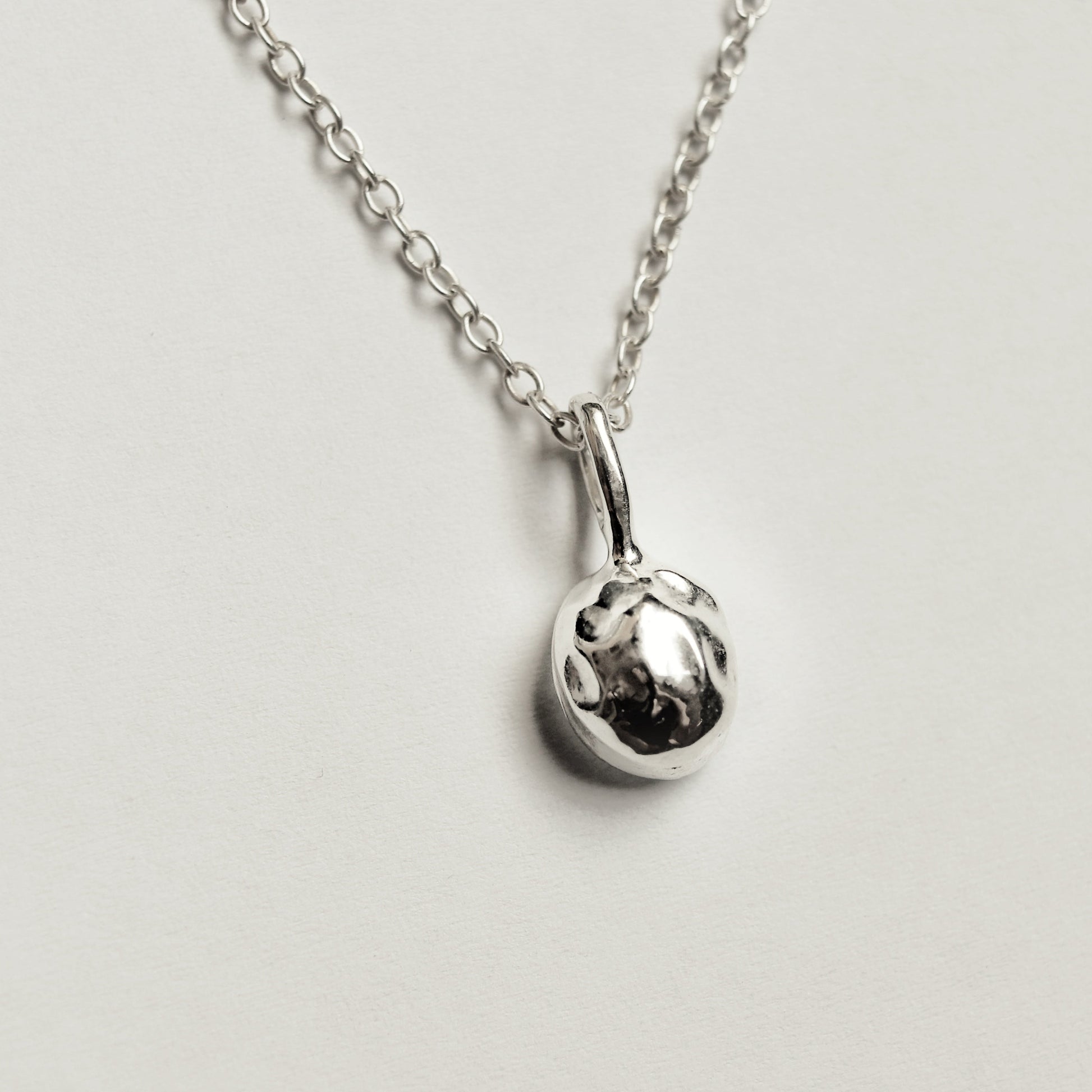 A silver chain necklace with a small, polished spherical pendant, photographed against a plain light gray background.