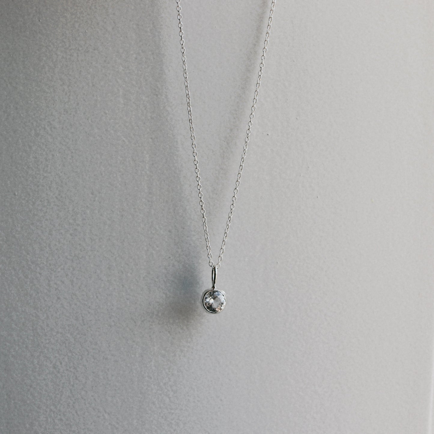 A delicate silver chain necklace with a small, textured silver bead pendant, displayed against a neutral light gray background.