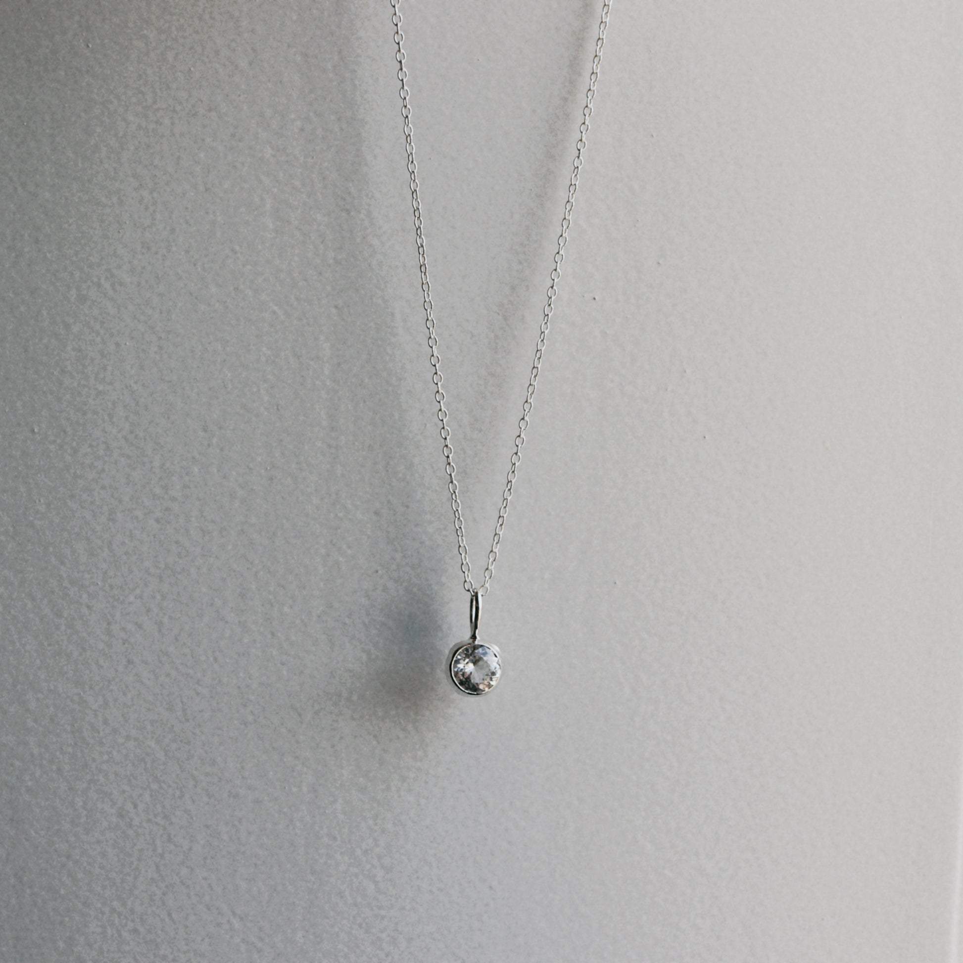 A delicate silver chain necklace with a small, textured silver bead pendant, displayed against a neutral light gray background.