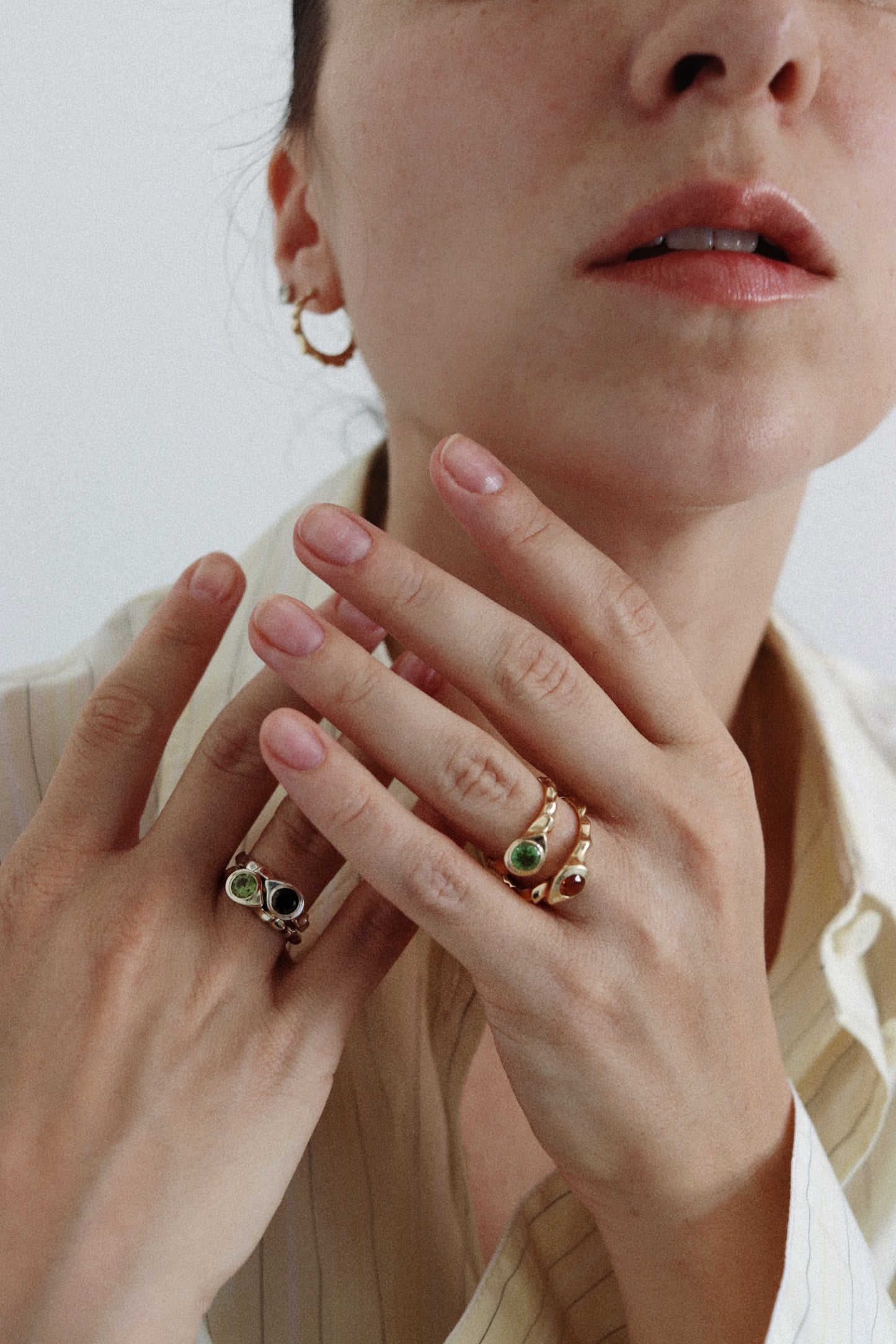 Close-up of a woman's hands wearing gold rings with green and black stones, against a soft light background.