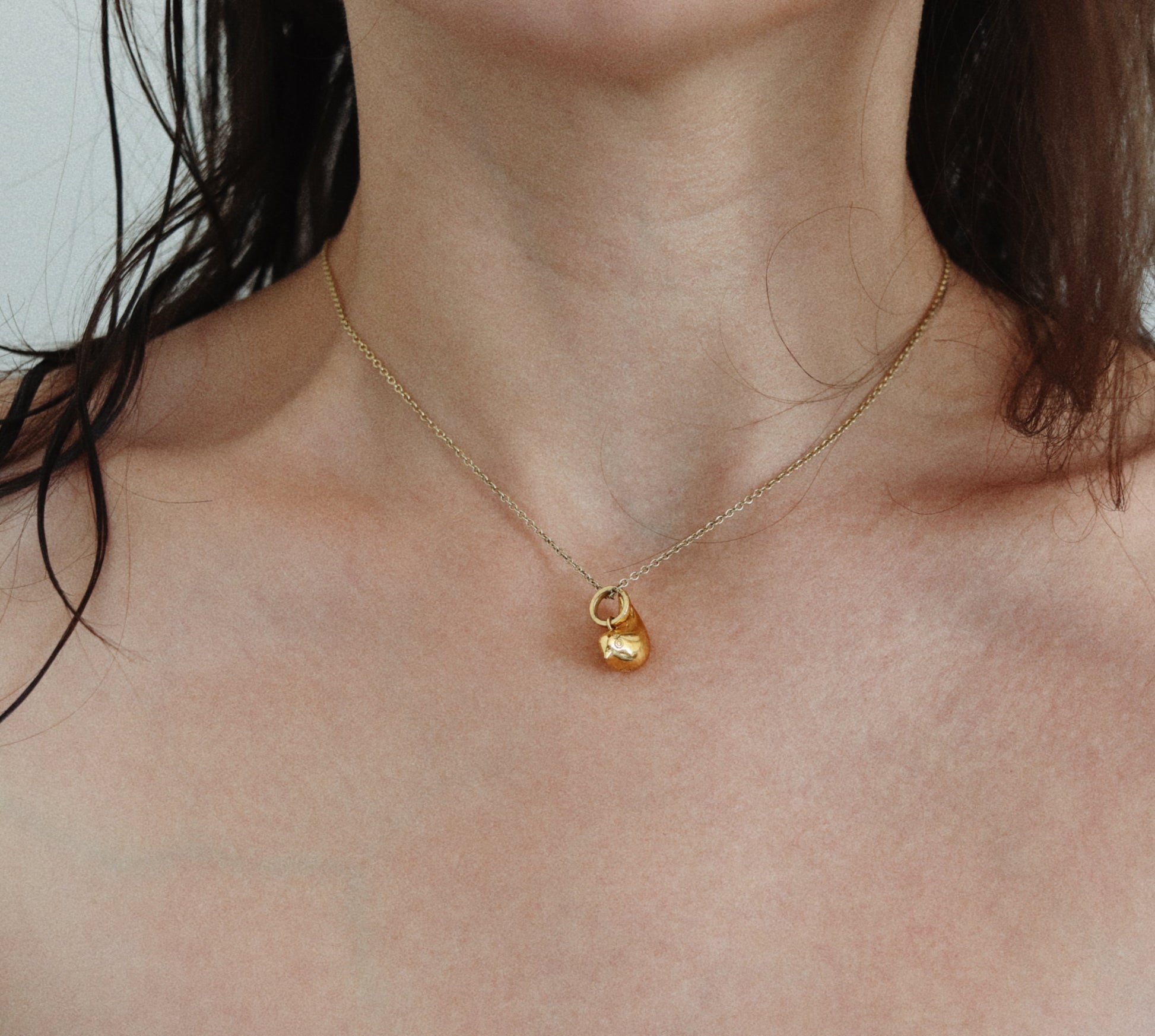 A close-up of a model's neck and chest wearing a delicate gold chain necklace with a small, polished gold padlock pendant.