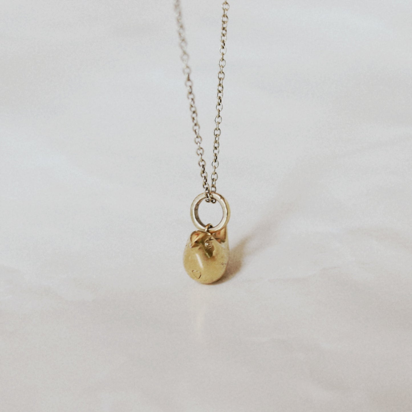 A delicate gold chain necklace with a small, polished gold bird pendant resting on a light, textured white surface.
