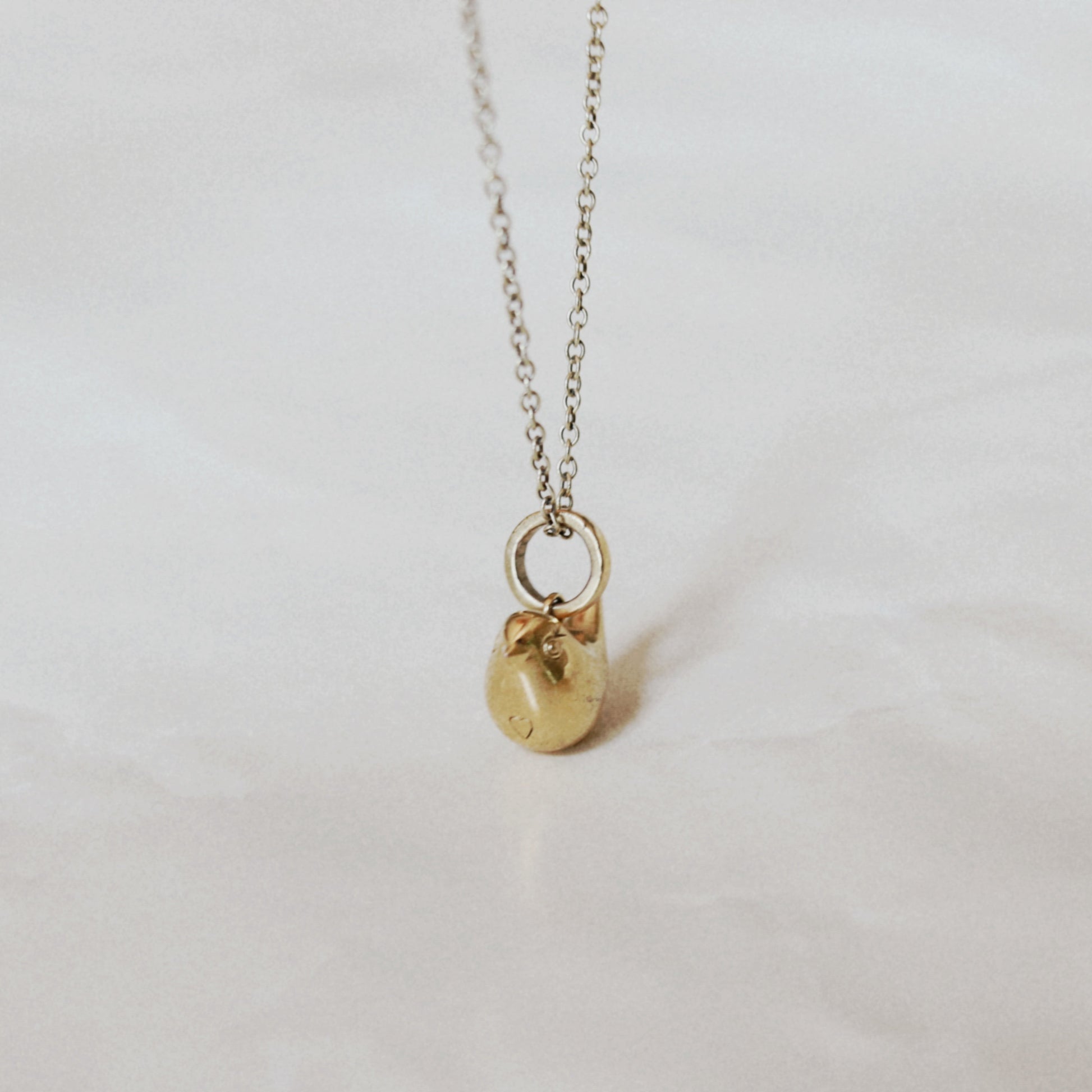 A delicate gold chain necklace with a small, polished gold bird pendant resting on a light, textured white surface.