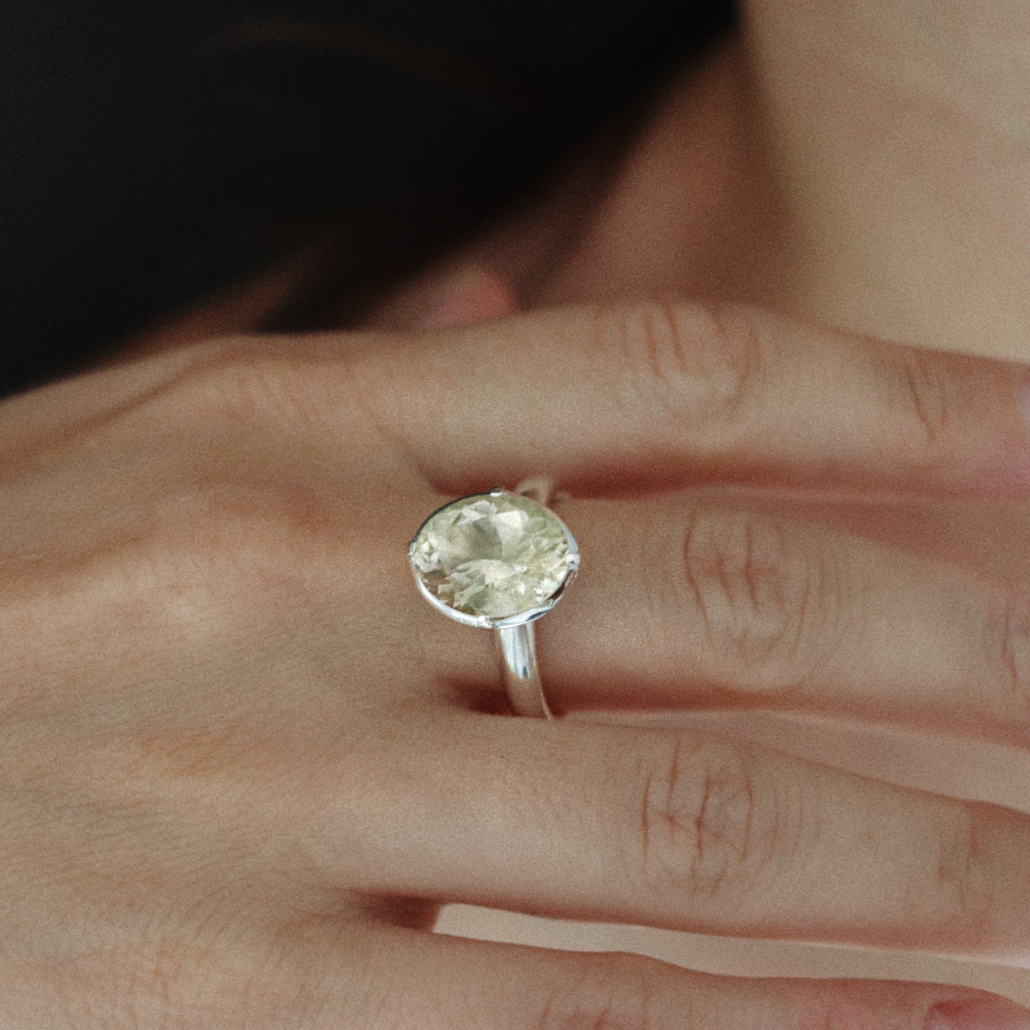A close-up of a hand wearing a silver ring with a large oval clear gemstone.