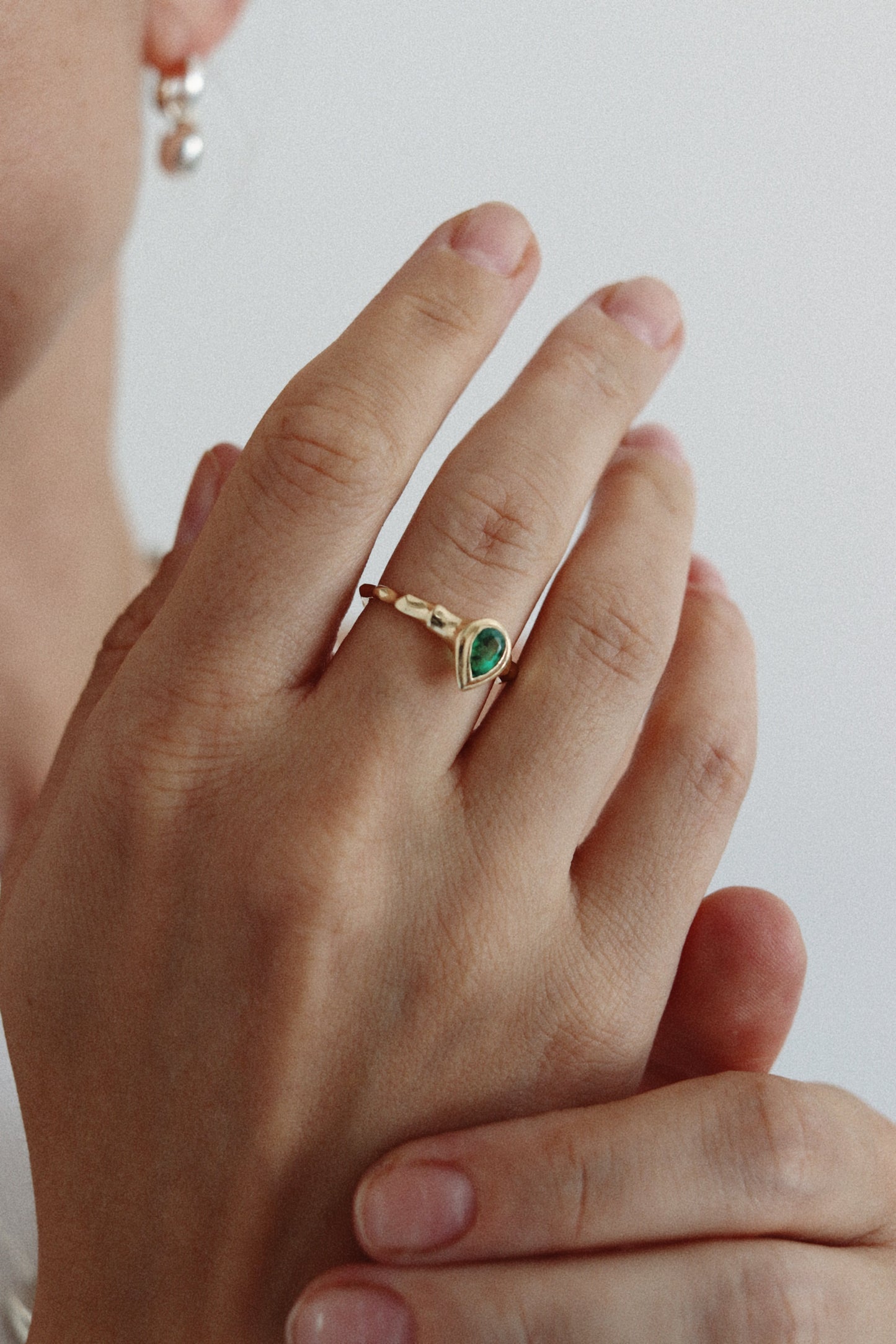 A close-up of a person's hand wearing a delicate gold ring with a small green marquise-cut gemstone.