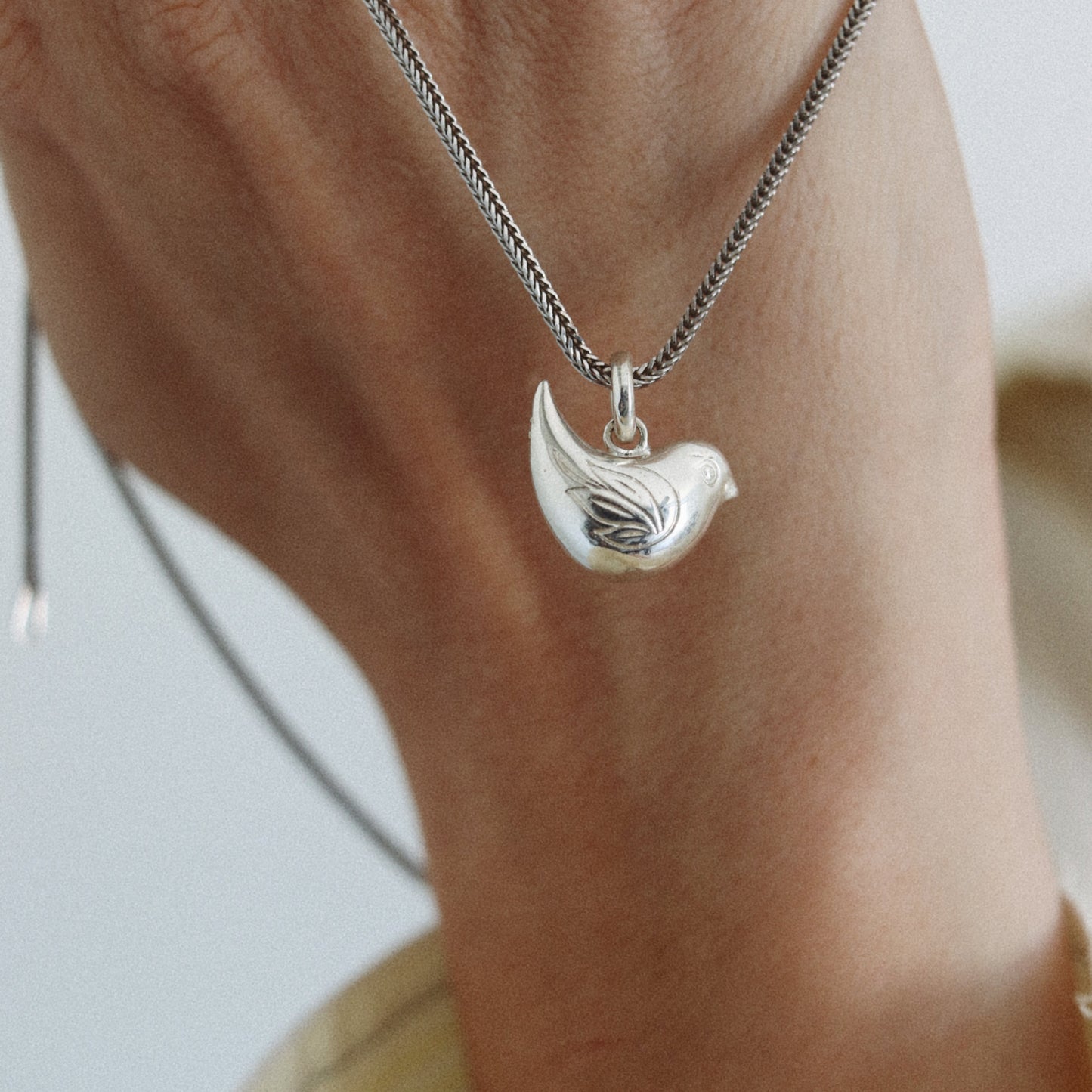 A close-up of a person's wrist wearing a silver chain necklace with a small bird-shaped pendant.