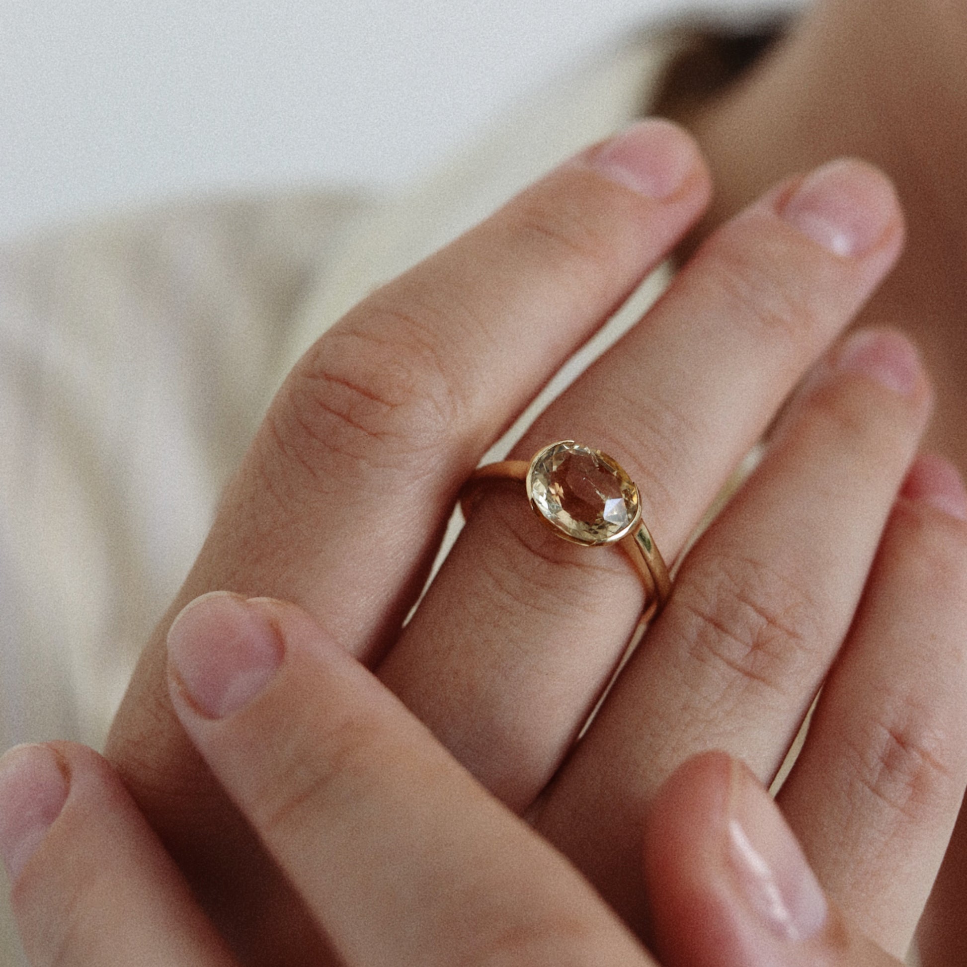 A gold ring with a round, faceted peach-colored gemstone worn on a person's finger, shown in a close-up lifestyle shot.