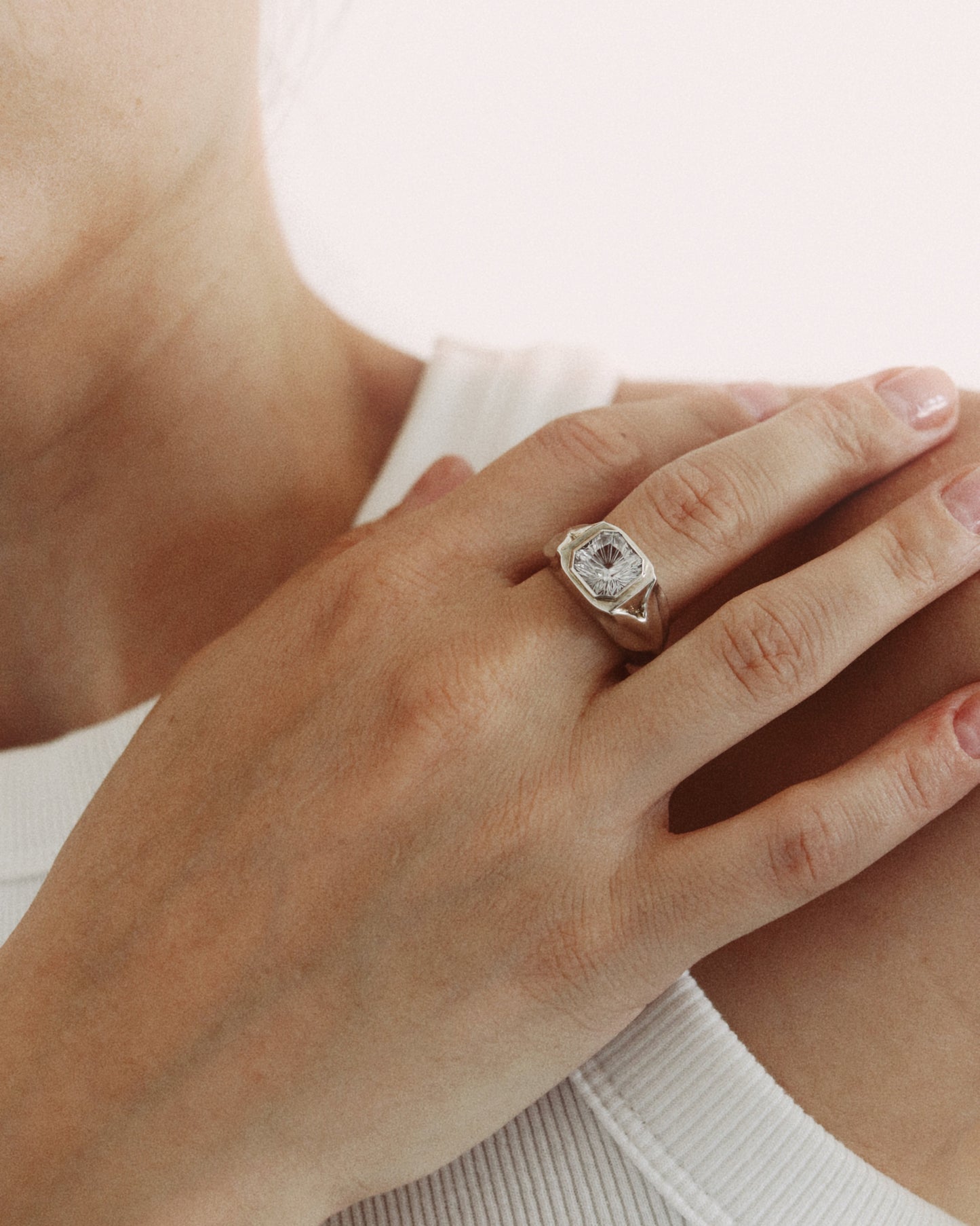 A close-up of a person's hand wearing a silver-toned ring with a marquise-cut clear gemstone, set against a soft, light background.