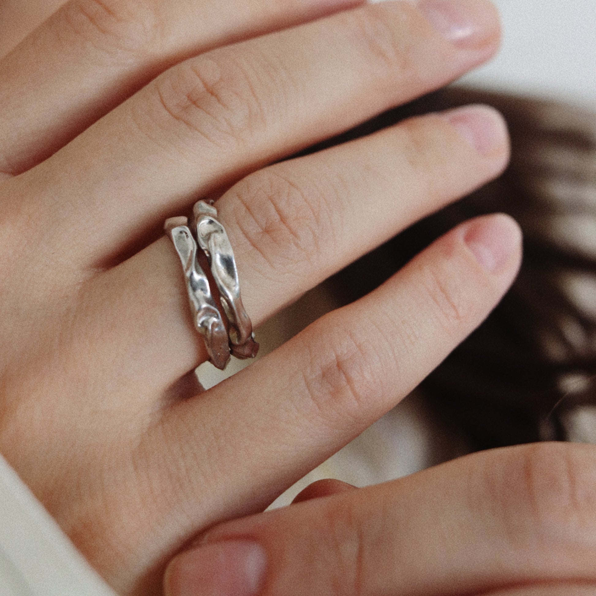 A close-up of a person's hand wearing two thin silver rings with textured, twisted patterns.