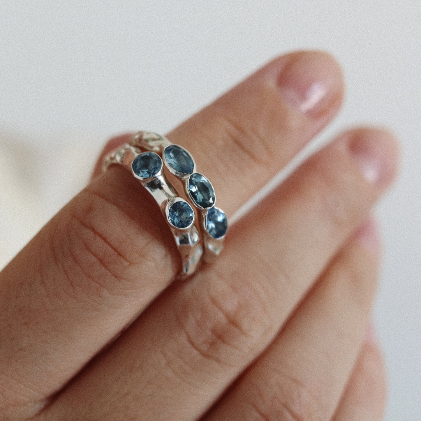 A close-up of a hand wearing a silver ring with three oval-cut blue gemstones.