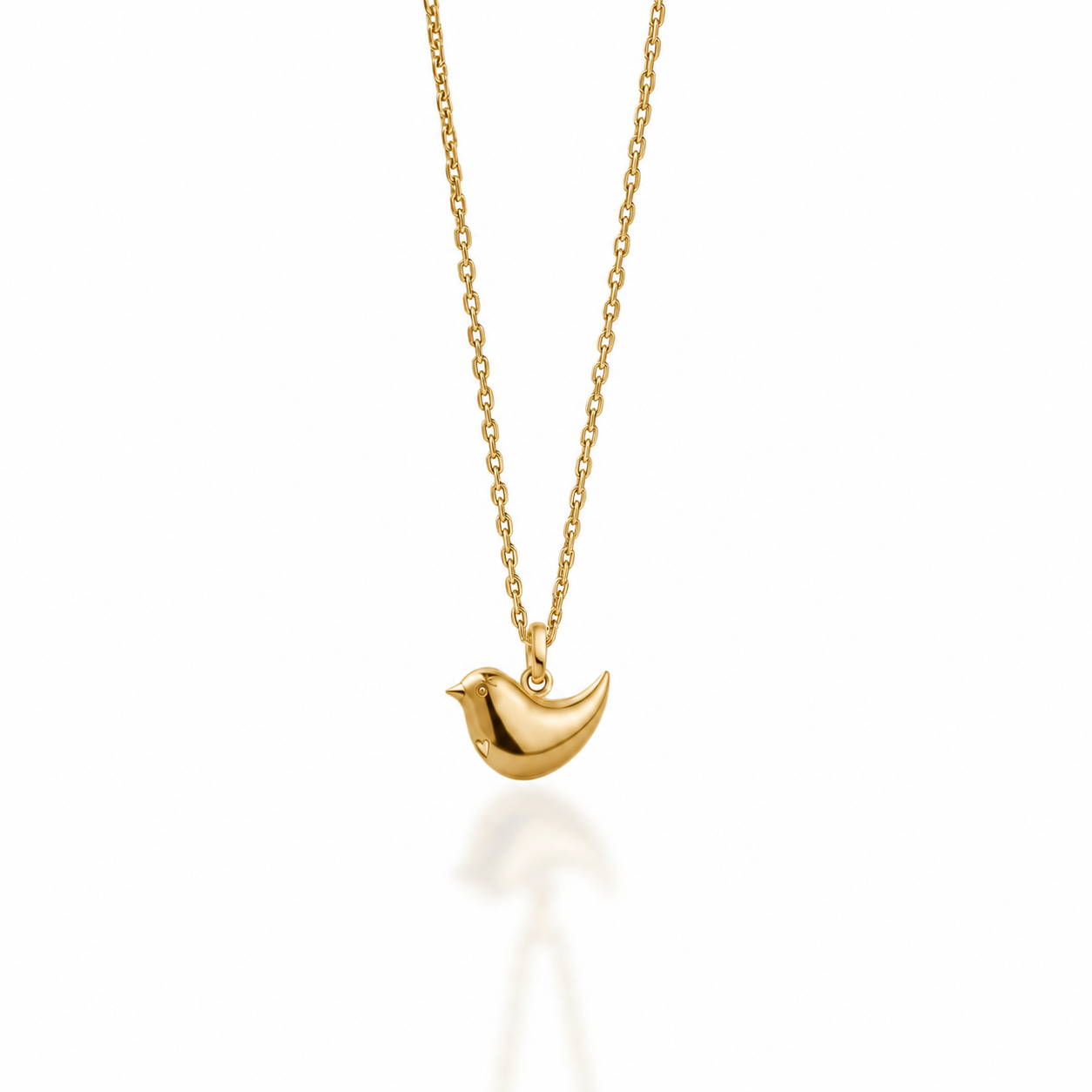 A delicate gold chain necklace featuring a small, polished gold bird pendant, shown against a clean white background with a soft reflection below.