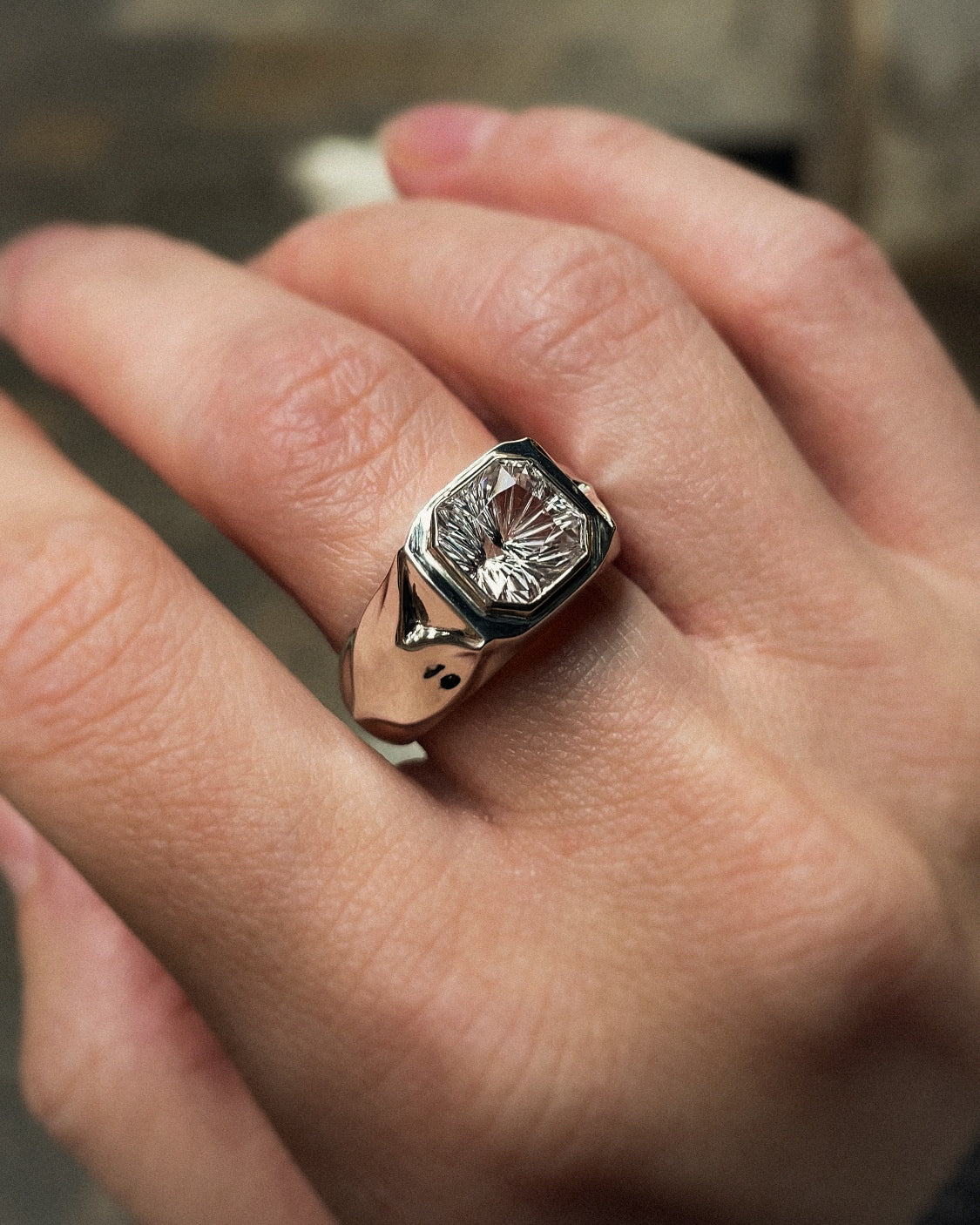 Close-up of a hand wearing a ring with a diamond on a blurred background