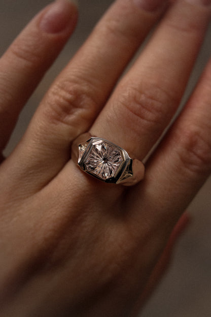 Close-up of a hand wearing a ring with a large diamond on a neutral background