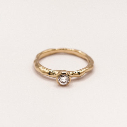 Gold ring with a diamond on a light beige background