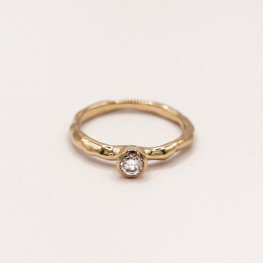 Gold ring with a diamond on a light beige background
