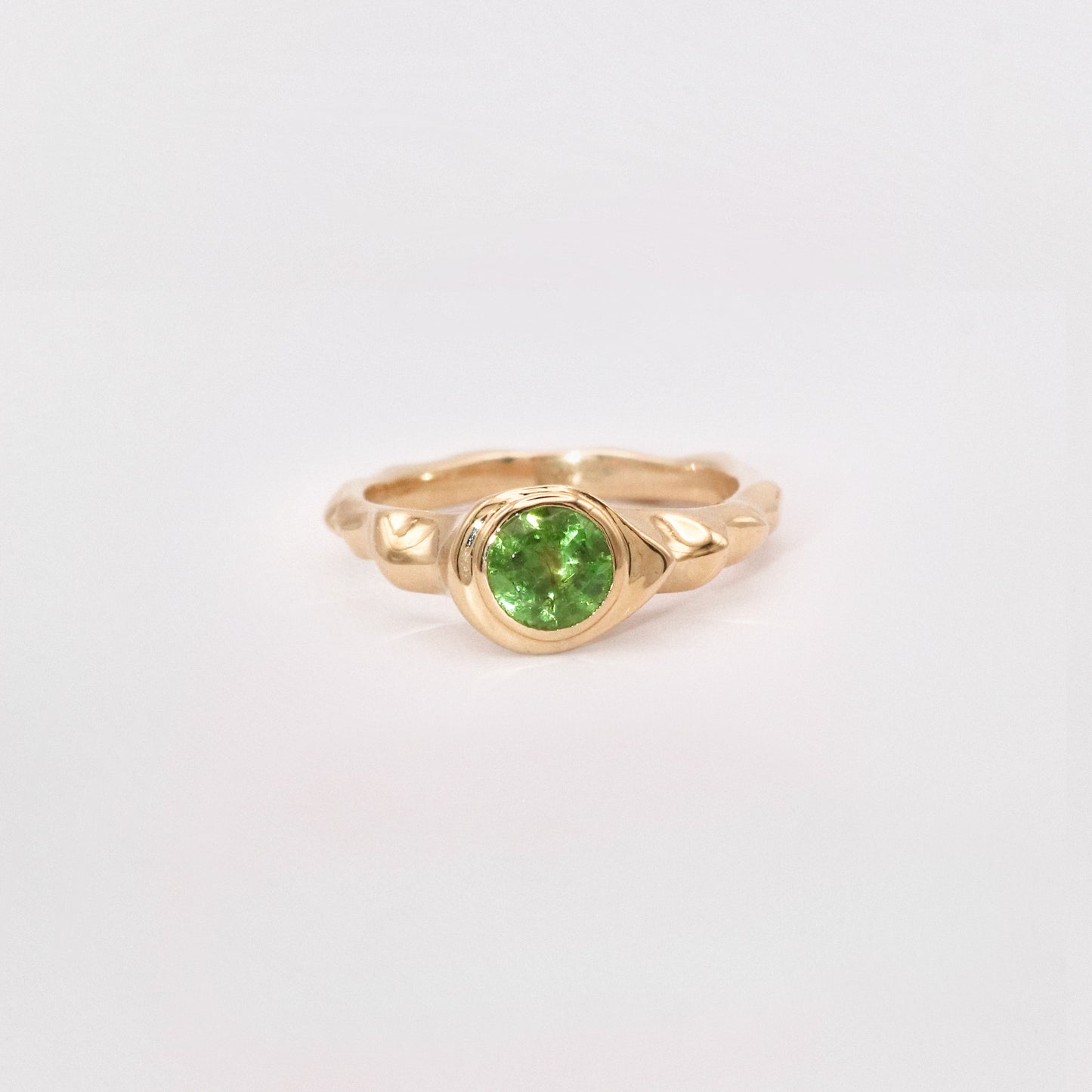 Gold ring with a green gemstone on a light gray background
