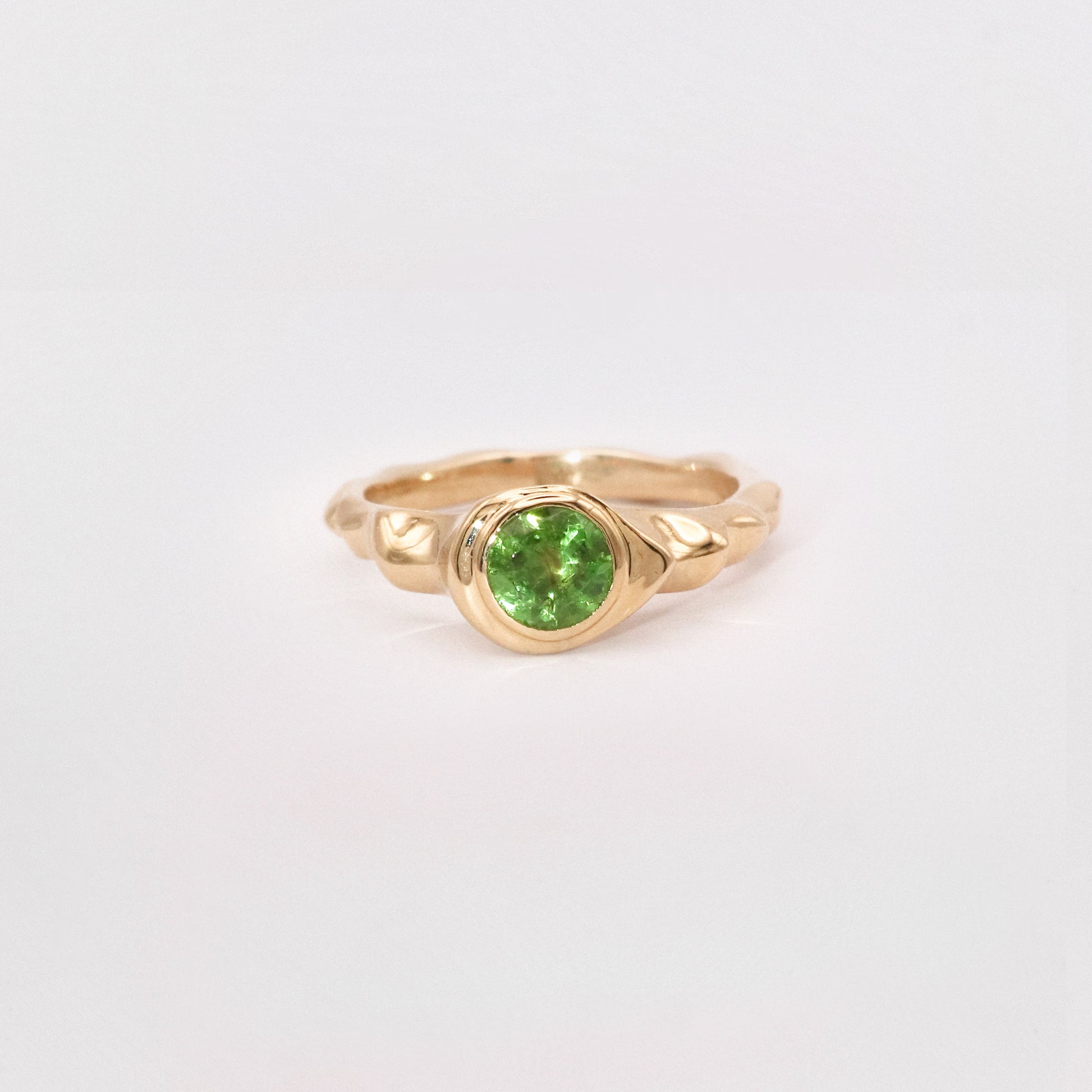 Gold ring with a green gemstone on a light gray background