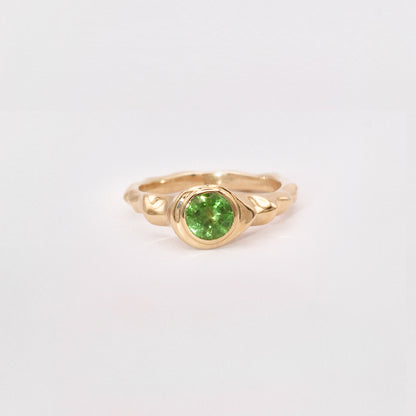 Gold ring with a green gemstone on a light gray background