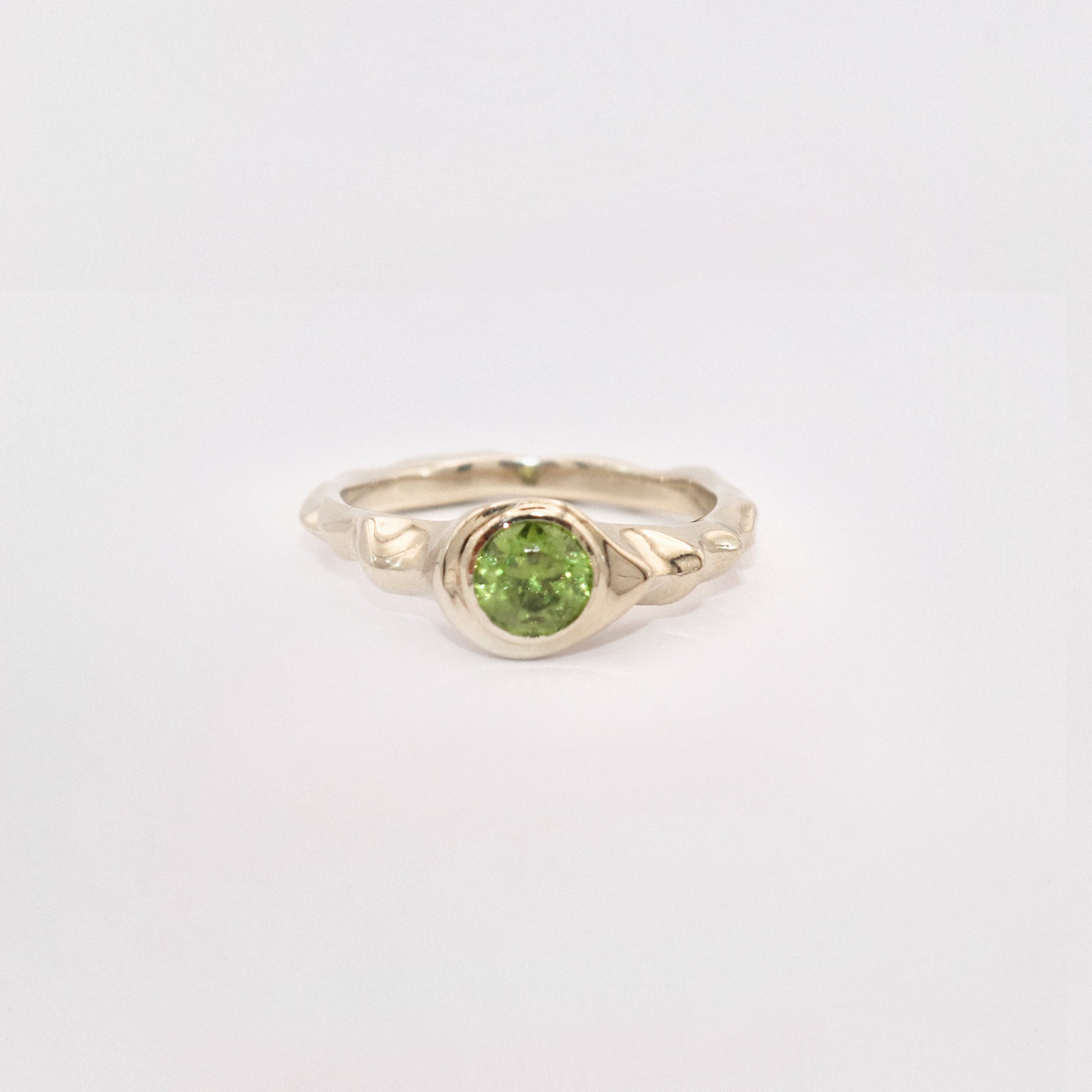 Gold ring with a green gemstone on a light gray background