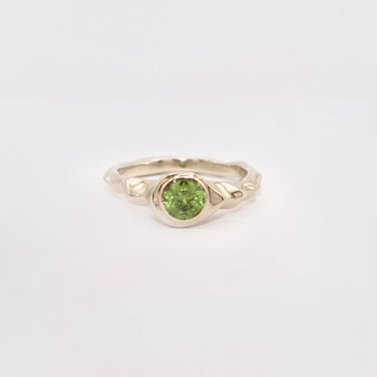Gold ring with a green gemstone on a light gray background