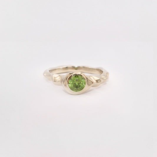 Gold ring with a green gemstone on a light gray background