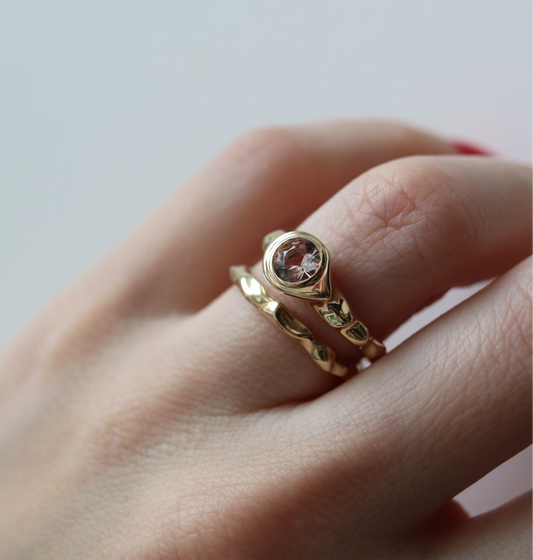 Gold ring with a gemstone on a person's finger against a neutral background