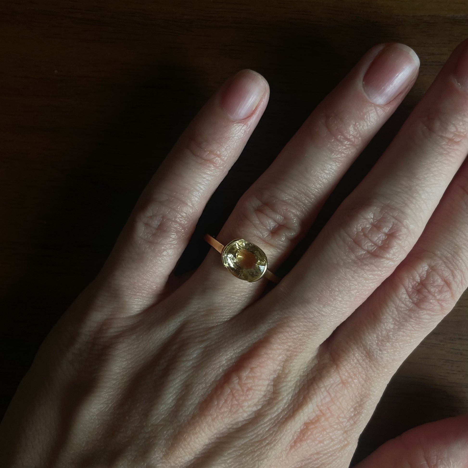 Gold ring with a yellow gemstone on a person's finger against a wooden background