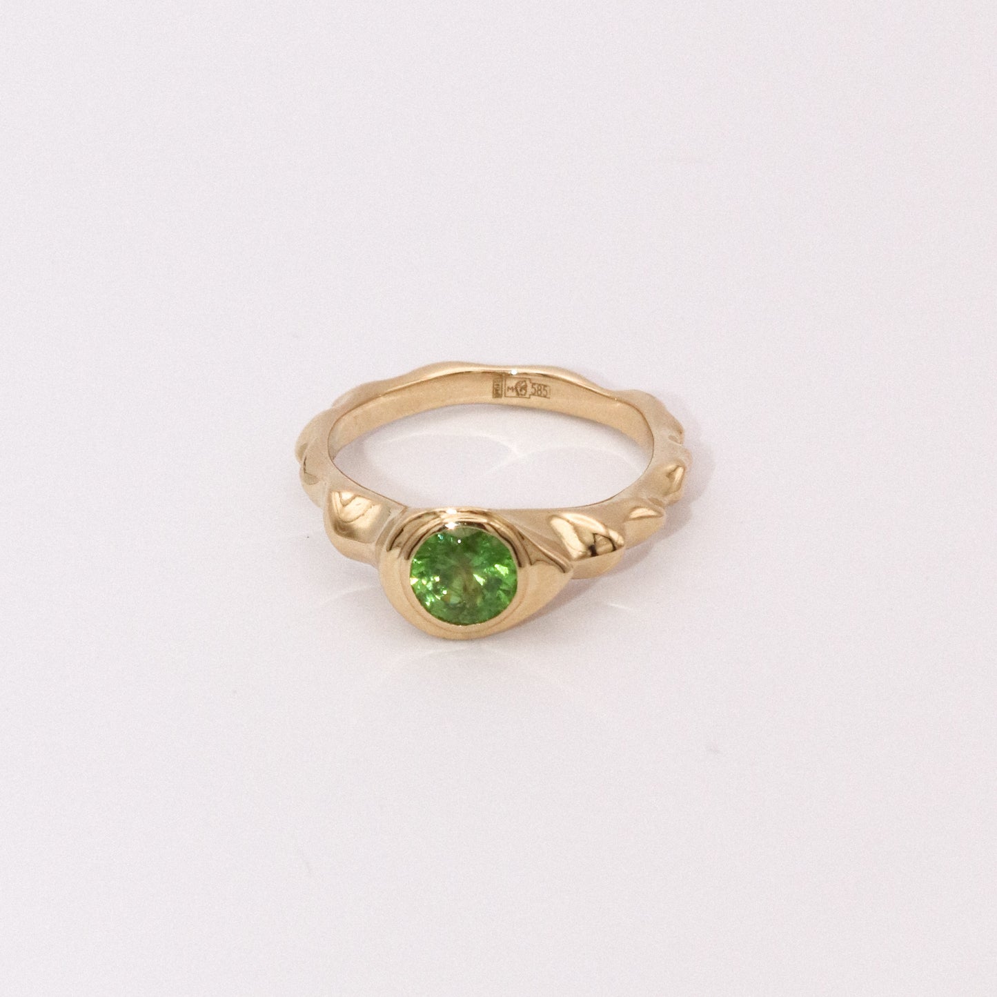 Gold ring with a green gemstone on a light gray background
