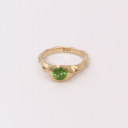 Gold ring with a green gemstone on a light gray background
