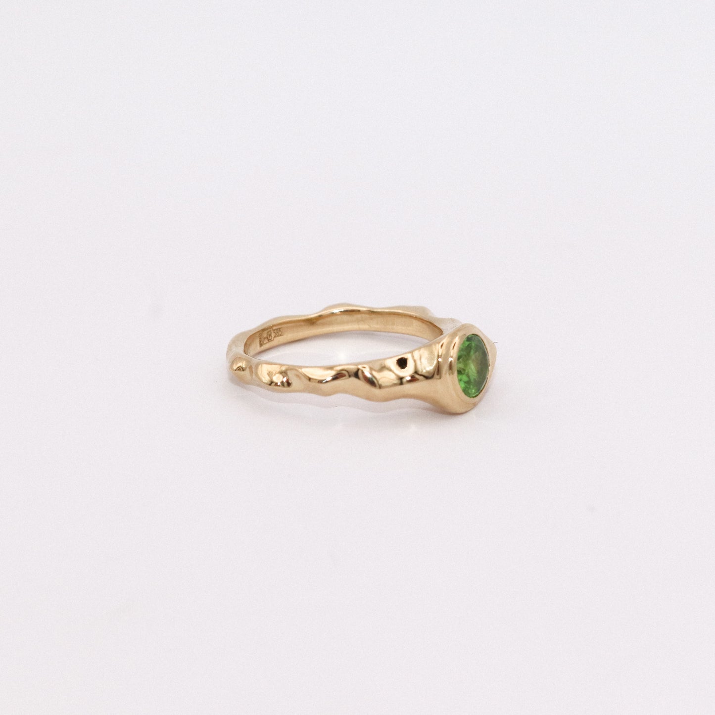 Gold ring with a green gemstone on a light gray background