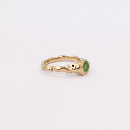 Gold ring with a green gemstone on a light gray background