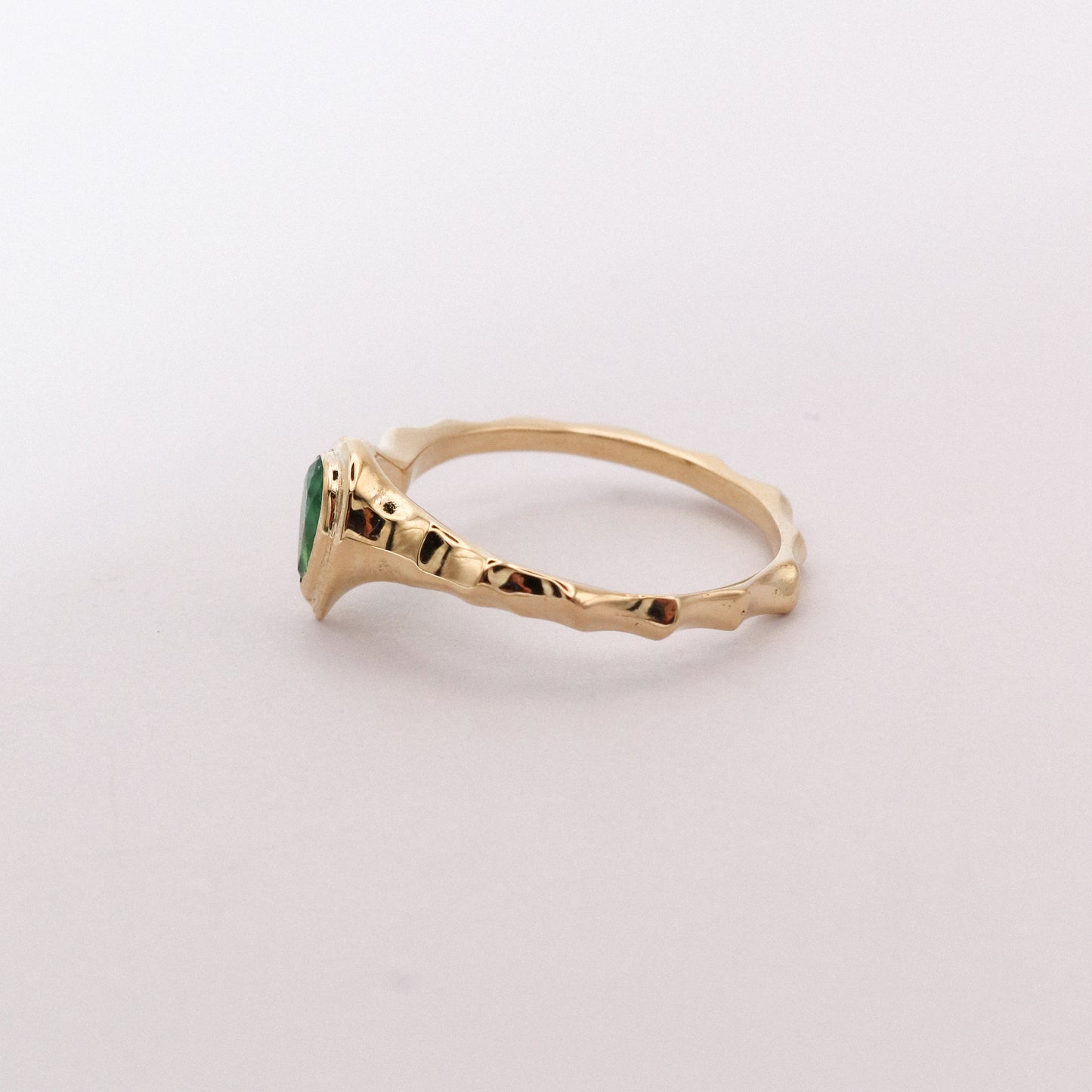 Gold ring with a green gemstone on a light gray background