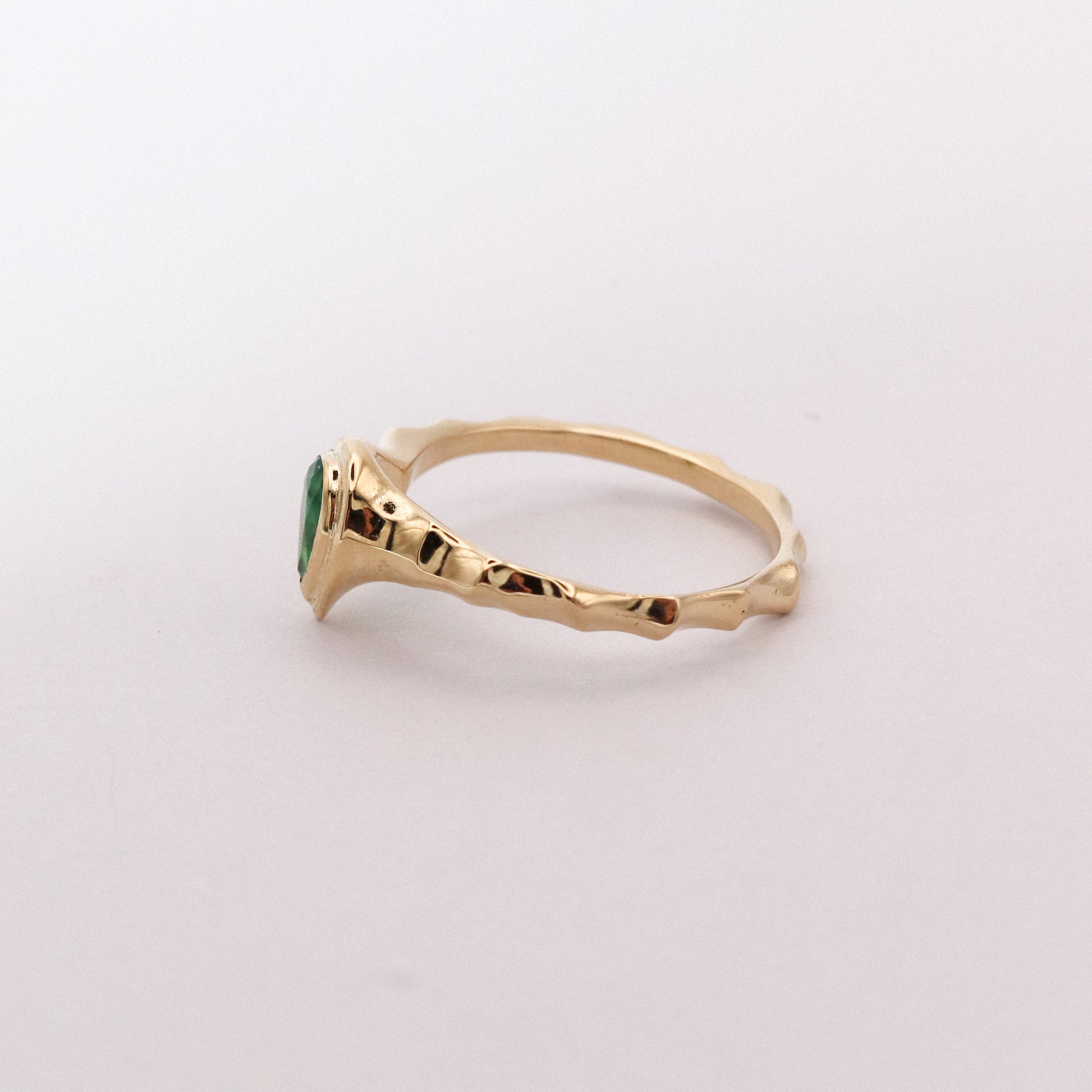 Gold ring with a green gemstone on a light gray background