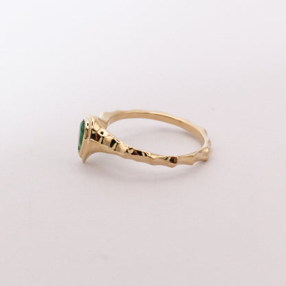 Gold ring with a green gemstone on a light gray background